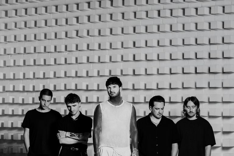 Black-and-white promotional photo of post-hardcore band Chiodos posing in dark outfits in front of a textured white block wall.